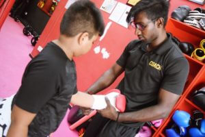 Coach Krishna assisting a young boxer with putting on their boxing glove.